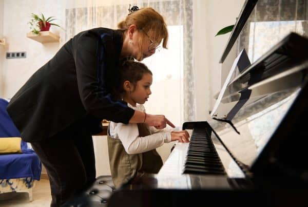 A mature woman piano teacher and a little girl student playing the piano.