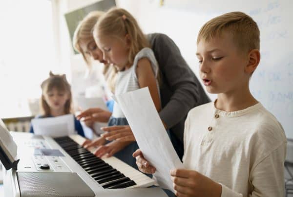 A group of children playing music on a keyboard with their teacher's supervision.